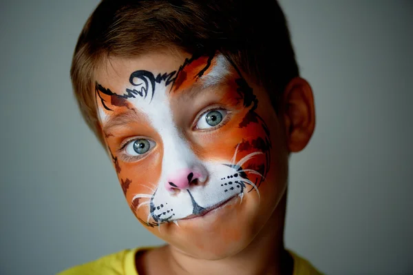 Years old boy with blue eyes  face painting of a cat or  tiger. Orange. — Stock fotografie