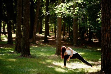 Young beautiful red-haired girl does yoga in Park on green background. .