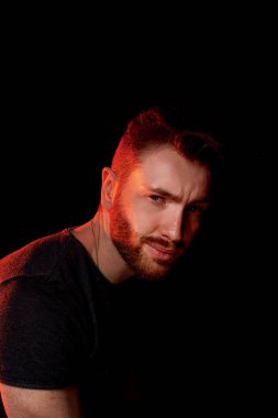 Kırmızı bir lambanın ışığında, karanlık bir arka planda vahşi bir adam..