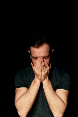 Siyah arka plandaki bir adam elleriyle yüzünü kapatır. Umutsuzluk atmosferi, keder