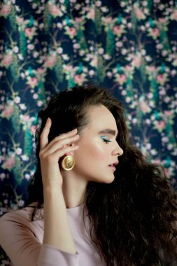 Büyük altın küpeli uzun kıvırcık saçlı güzel bir kız. Güzellik, tarz ve moda..