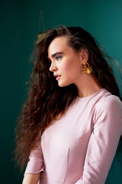 Pembe elbiseli, kıvırcık saçlı güzel bir kız. Stüdyodaki yeşil duvarların arkasında, profilden