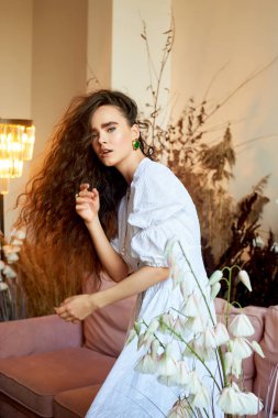 Beyaz uzun elbiseli, uzun kıvırcık saçlı güzel bir kız, dinamik bir şekilde hareket ediyor. Mısır gevrekli fotoğraf stüdyosu. Moda ve güzellik.