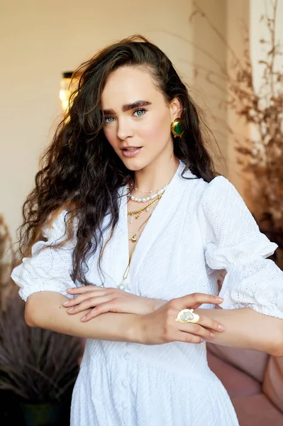 Una hermosa chica con el pelo largo y rizado en un vestido largo blanco, se mueve dinámicamente. Estudio fotográfico con cereales. Moda y belleza. — Foto de Stock