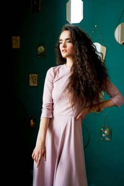 Pembe elbiseli, kıvırcık saçlı güzel bir kız. Stüdyodaki yeşil duvarların arkasında, profilden