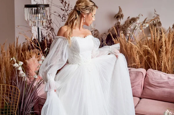 The bride dances and whirls in a white curvy dress. Its a beautiful studio. European type of appearance, blonde.