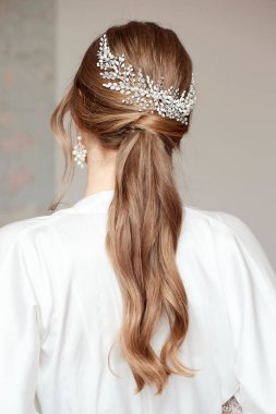 Zarif, uzun saçlı, güzel bir gelin. Saçında aksesuar olan düğün saç stili. Işık arkaplanındaki yakın plan portresi