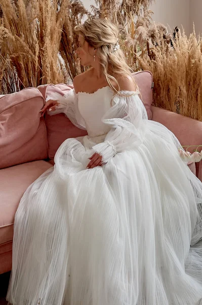 新娘站在漂亮的粉色沙发上.一间用谷物装饰的房间。华丽的衣服. — 图库照片
