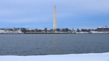 Washington Anıtı, Washington D.C. 'deki dalgalanan gelgit havzasından bakıldığında karla kaplı bir bankın üzerinde duruyor. Sakin, soğuk bir kış manzarası..
