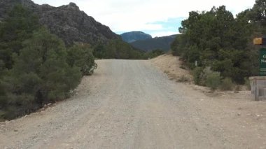 Great Basin National Park entrance sign and gravel road are revealed in this dolly out shot against a rugged mountain backdrop.