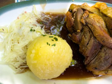 Çıtır derili Alman schweinehaxe, büyük bir patates köftesi, sos ve lahana turşusu.