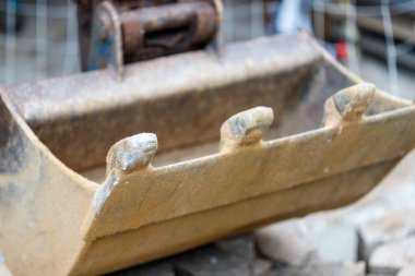 Yakın plan, sığ alan derinliği, küçük bir kazıcı kovasının yıpranmış, paslı dişleri ve metaline odaklanır..