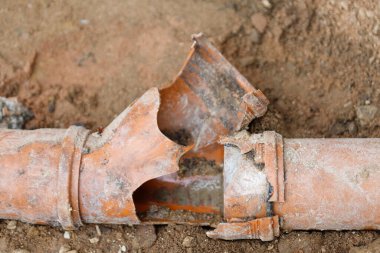 Kırık bir turuncu plastik boru toprakta yatıyor, büyük bir kısmı parçalanmış ve ayrılmış, iç kısmı ortaya çıkıyor..