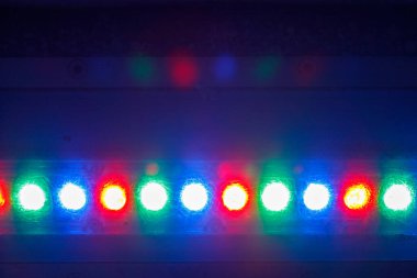 Koyu mavi arkaplan üzerinde kırmızı, yeşil ve mavi renklerde beyaz ve sarı renklerde ışık saçan yatay bir LED satırı.