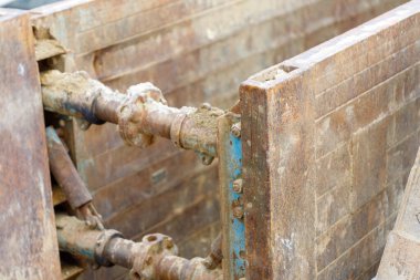 Ağır çelik borular bir siperdeki boruları destekliyor. Pas ve kir yapıları görünür cıvatalar ve flanşlarla kaplıyor..