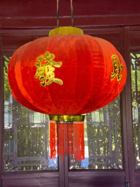 Altın sarısı bir Çin feneri ahşap bir yapının önünde duruyor ve yeşilliği bulanıklaştırıyor..