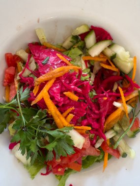 Domatesli, salatalıklı, salatalıklı, marullu, doğranmış havuçlu ve maydanozla süslenmiş kırmızı lahanalı renkli bir salata..