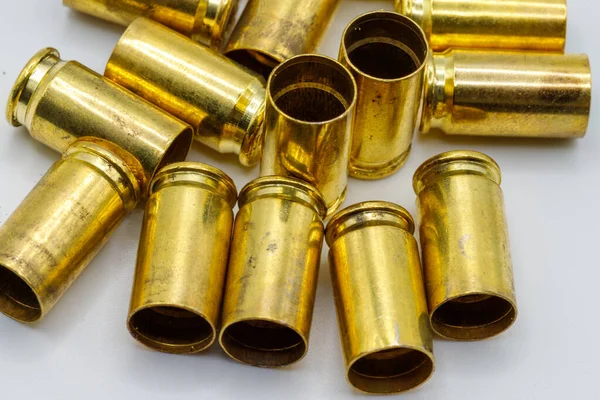 Mermi kovanları beyaz bir yüzeye saçılmış. Kovanların çoğu sağlam ve bazı küçük lekelerle karakteristik altın renklerini sergiliyorlar..