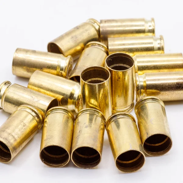 Kullanılmış pirinç mermi kovanları beyaz bir yüzeye saçılmış, sıcak, altın gibi metalik bir parıltı ve biraz da kir gösteriyor..