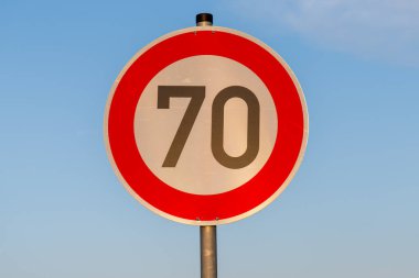 Yuvarlak yol işareti açık mavi gökyüzüne karşı saatte 70 kilometre hız limitini gösteriyor.