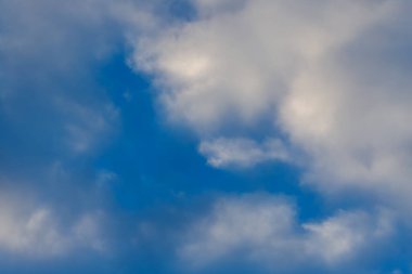 Kabarık beyaz kümülüs bulutlarıyla mavi gökyüzü, huzurlu bir gündüz atmosferi yaratıyor.