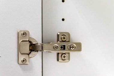 Metal dolap menteşesi vikli beyaz bir mobilya paneline bağlı.