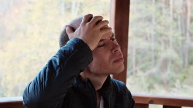 Orta yaşlı bir adam, şiddetli baş ağrısı belirtileri gösteren acı dolu bir ifadeyle kafasına dokunuyor. Sağlık, stres ve tıbbi içerik için mükemmel bir 4K videosu. Yüksek kalite 4k görüntü