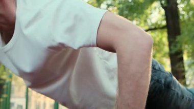 A middle-aged man in a white tank top performs push-ups on a sports ground. Perfect 4K video for fitness, exercise, and healthy lifestyle content. High quality 4k footage