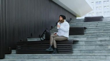 Park merdivenlerinde oturan kadın termostan çay içiyor. Kentsel Rahatlama. Yüksek kalite 4k görüntü