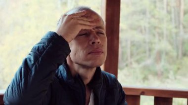 Orta yaşlı bir adam, şiddetli baş ağrısı belirtileri gösteren acı dolu bir ifadeyle kafasına dokunuyor. Sağlık, stres ve tıbbi içerik için mükemmel bir 4K videosu. Yüksek kalite 4k görüntü