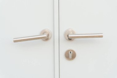 Arka plan olarak iki gümüş kapı tutacağı ya da kolu ve ayrılmış anahtar deliği olan beyaz kapı veya kapı yaprağı kullanılır.