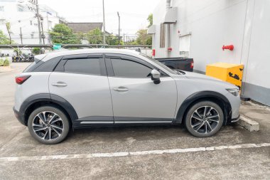 Sağ tarafı manzaralı küçük gri spor bir hatchback arabası alışveriş merkezinin açık otoparkına park ediyor..