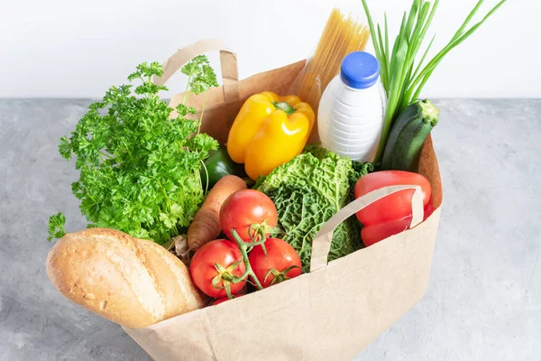 Gri masada içi taze organik sebze ve market ürünleriyle dolu kağıt alışveriş kutusu. Çevre alışverişi ya da yiyecek teslimatı kavramı.