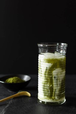 Siyah arka planda uzun bir bardakta yeşil kibritli buzlu latte. Matcha tea 'nın sakin yaşamı.