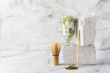 Modern dengeli gri beton arka planda uzun bir bardakta yeşil kibritli buzlu latte. Matcha çayının modern hayatı.