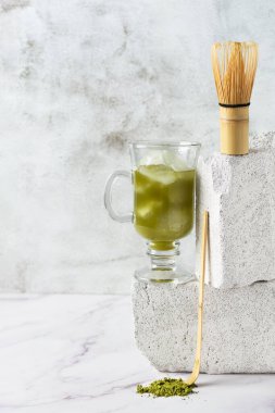 Modern dengeli gri arka planda uzun bir bardakta yeşil kibrit buzlu çay. Matcha çayının modern hayatı.