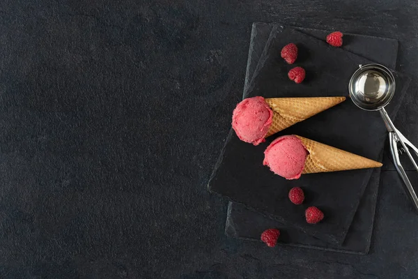 Raspberry ice cream in a waffle cones on black table top view. Summer refreshing sorbet.