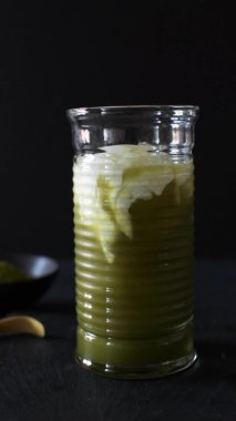 Siyah arka planda uzun bir bardakta yeşil kibrit buzlu latteye süt döküyorum..