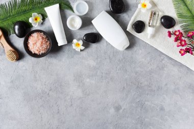 Masaj ve cilt bakımı için organik spa ürünleri. Temel yağ, nemlendirici ve siyah zen taşlarıyla gri beton arka planda üst görünüm. Spa tedavi arkaplanı.