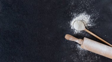 Tahta kaşıkta buğday unu ve siyah yüzey manzarası üzerinde merdane var. Tasarımınız için fırın arkaplanı.