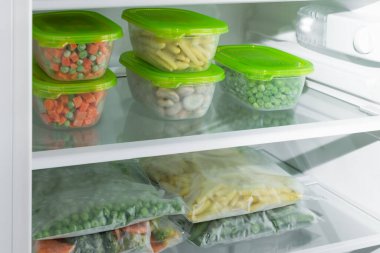 Buzdolabında farklı donmuş sebzeler olan plastik kaplar ve poşetler. Korunmuş sebzeler. Sağlıklı beslenme.