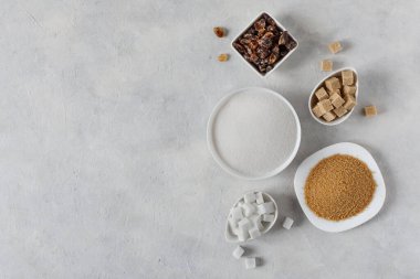 Çeşitli şeker çeşitleri. Gri arkaplanda üst görünümde farklı beyaz ve kahverengi şeker.