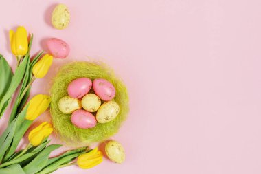 Bahar sarısı lale çiçekleri ve renkli Paskalya yumurtaları pastel pembe arka planda. Kopya alanı olan Paskalya arkaplanı.