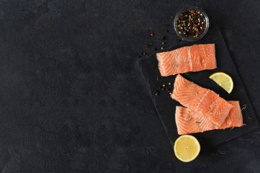 Kağıt baharatlı taze çiğ somon balığı filetosu ve siyah arka planda bir dilim limon. Sağlıklı beslenme omega 3 dolu..
