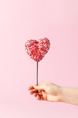 Balon şeklinde kalp şeklinde donutu olan yaratıcı kompozisyon ve pastel pembe arka planı olan kadınlar. Sevgililer Günü için yaratıcı pişirme.
