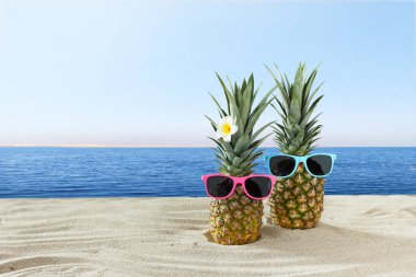 Mavi denizin üzerindeki kumlu sahilde güneş gözlüklü yaratıcı tropikal ananas çifti..