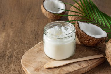 Jar of coconut butter and fresh coconuts with palm leaf on wooden background. Healthy vegan food.
