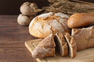 Dilimlenmiş bir somun ekmek ve ahşap masada diğer çeşitli ekmekler. Bir somun kepekli ekmek..