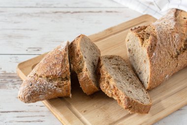 Beyaz ahşap masada dilimlenmiş bir somun ekmek. Bir somun kepekli ekmek..