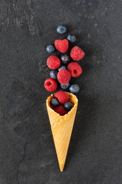 Böğürtlen ve ahududu karışımı siyah arka planda waffle dondurma külahında. Yaban mersinli yaratıcı kompozisyon.